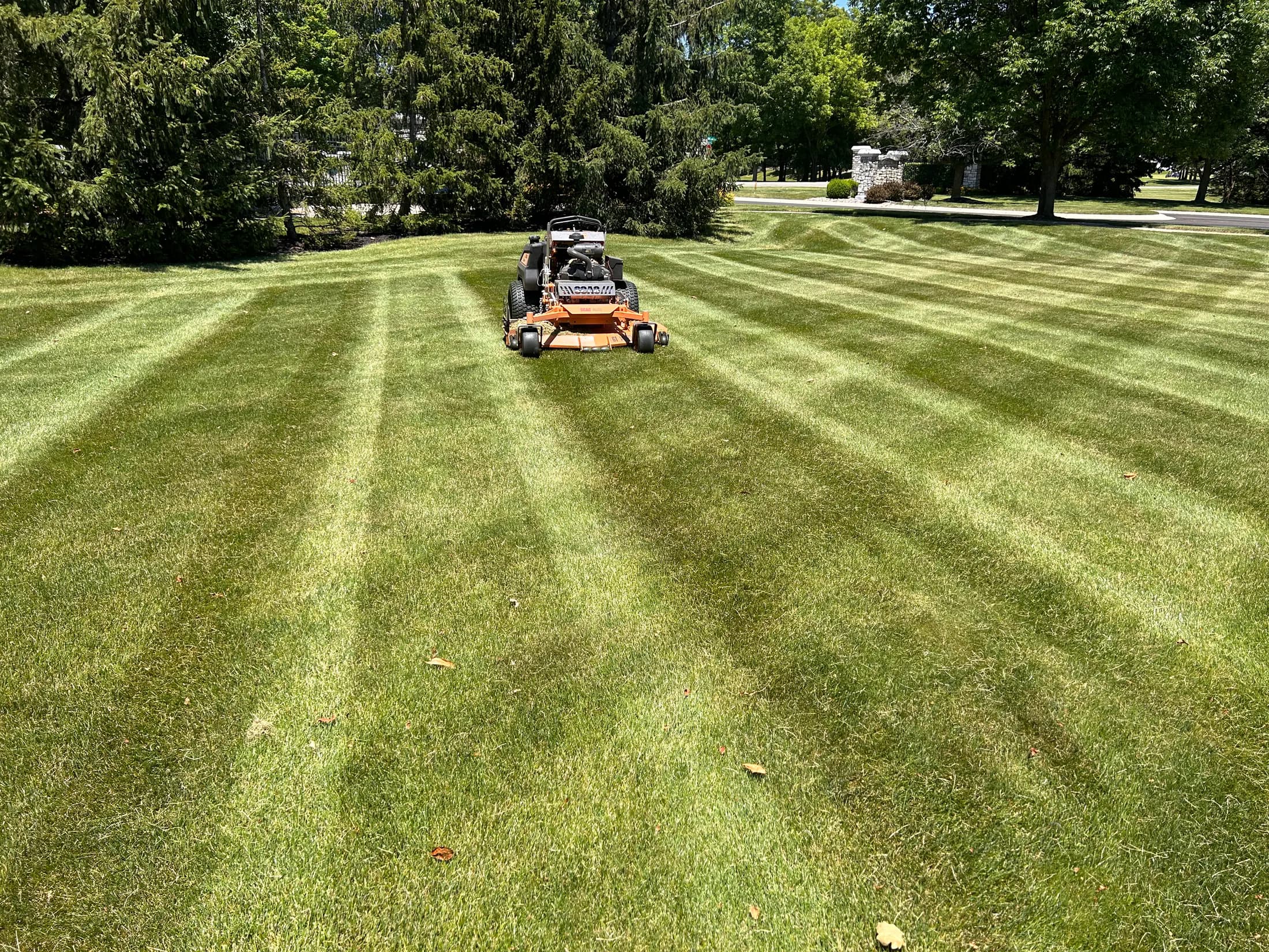 A commercial mower working across a broad striped lawn