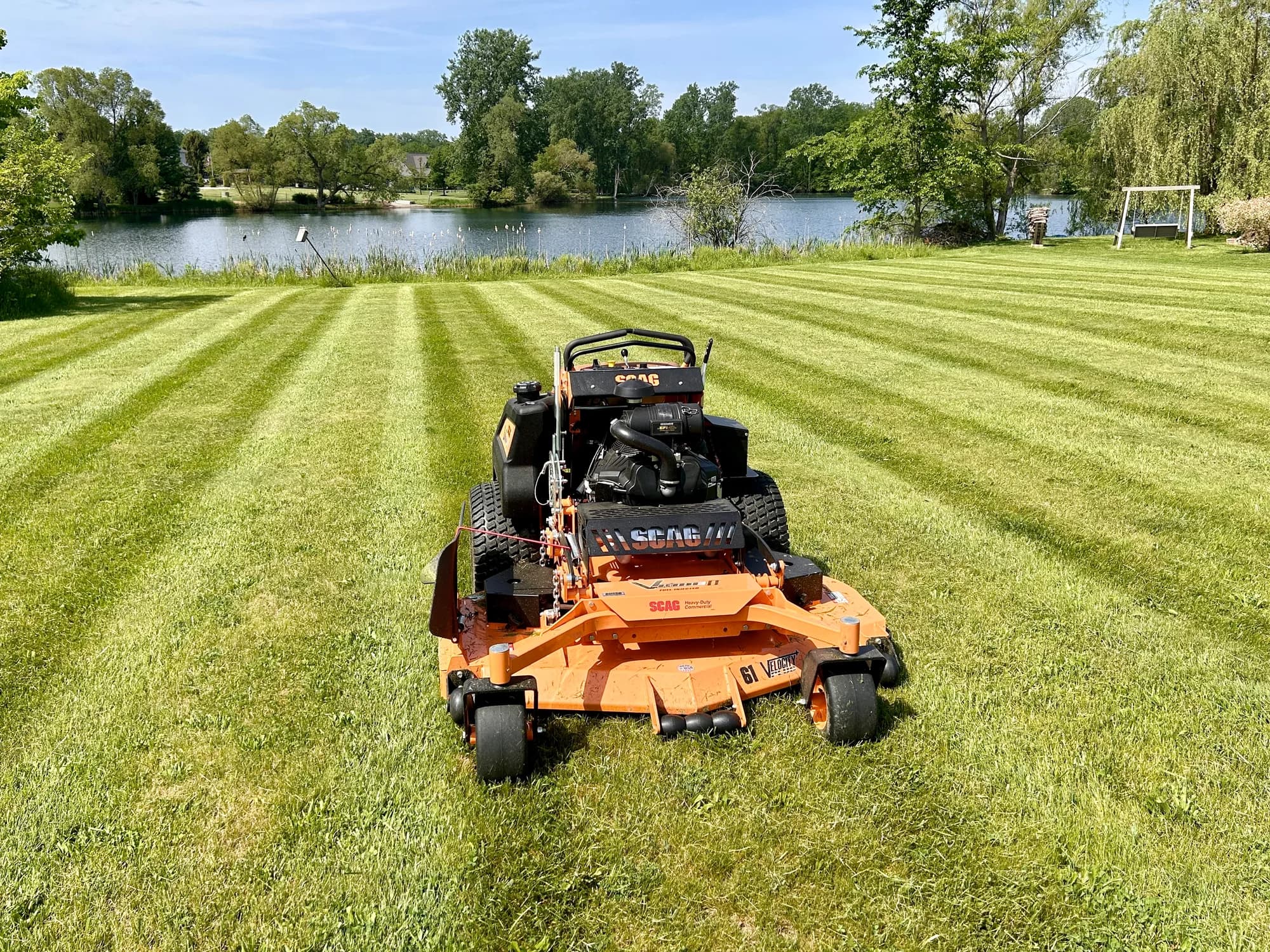 A commercial mower on a freshly cut lawn beside a pond